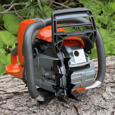 A Ripsaw RS572 - A ported Husqvarna chainsaw on a log with foliage in the background. The saw is shown with Ripsaw 4 point felling dogs and a Ripsaw Signature Series Exhaust.