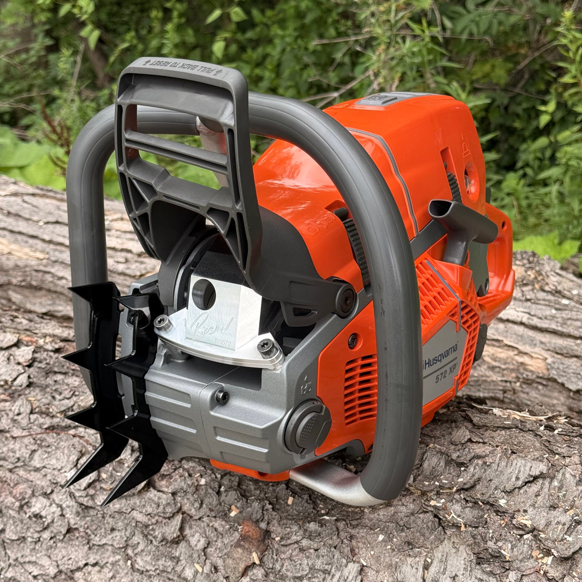 A Ripsaw RS572. A ported Husqvarna chainsaw with a bright orange body, gray handlebars, and a black front guard, resting on a log with green foliage in the background. The saw is shown with Ripsaw 4 point felling dogs and a Ripsaw Signature Series Exhaust.